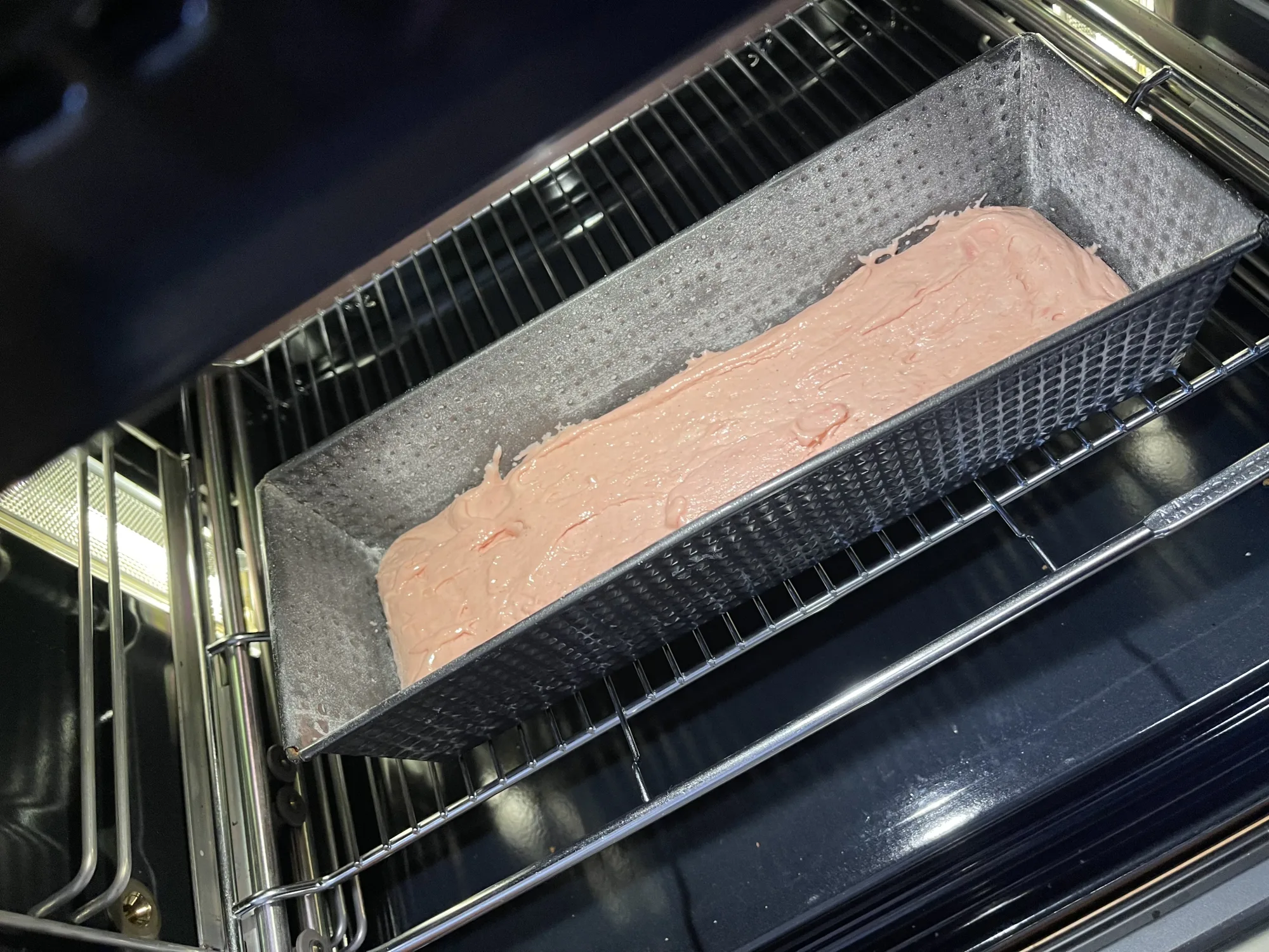Rosa Rührteig in einer grauen Kastenform auf dem Rost im Backofen, vor dem Backen für den Kuchen mit verstecktem Herz