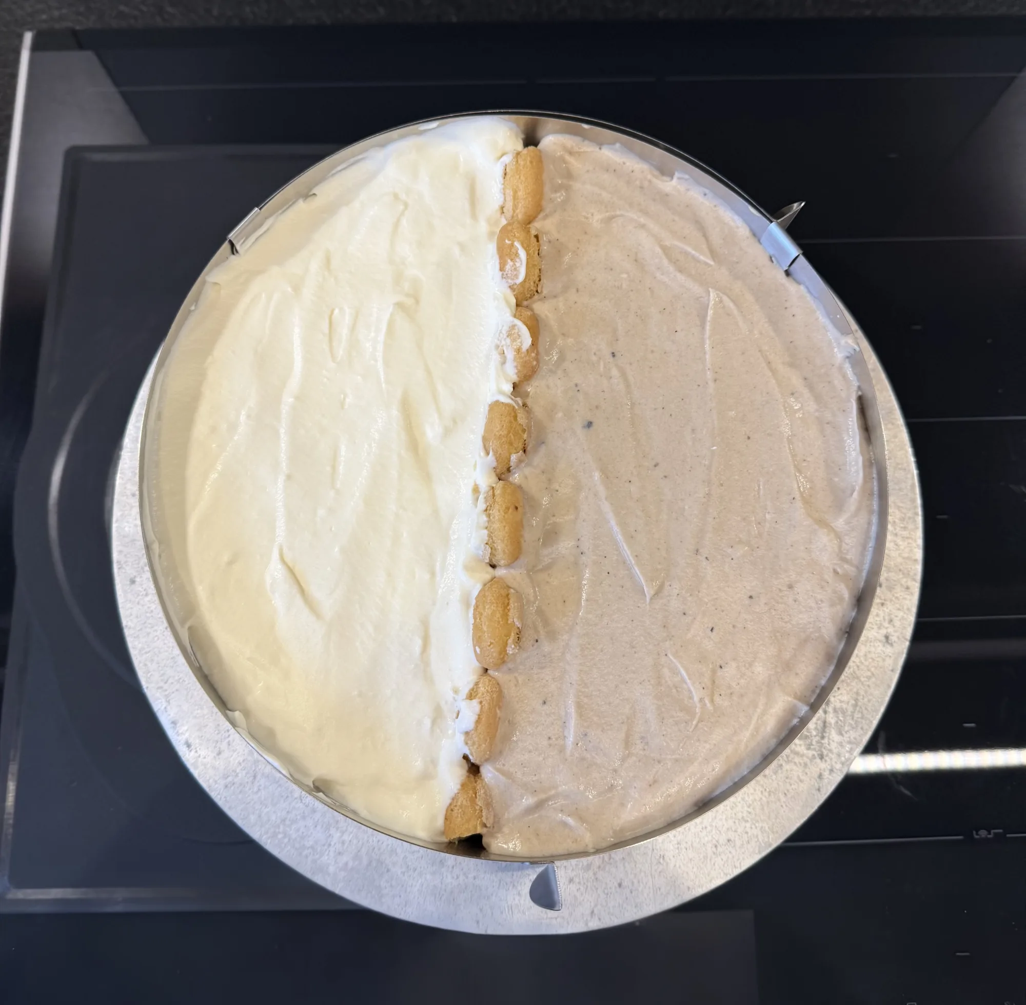 Sahnetorte halb/halb im Tortenring: links helle Sahnecreme, rechts beige Creme, getrennt durch eine Reihe Löffelbiskuits.