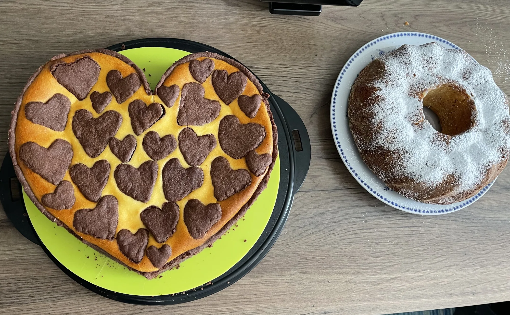 Herzförmiger Zupfkuchen mit dunklen Schokoteig-Herzen auf gelber Quarkmasse, daneben ein Gugelhupf mit Puderzucker auf blauem Teller