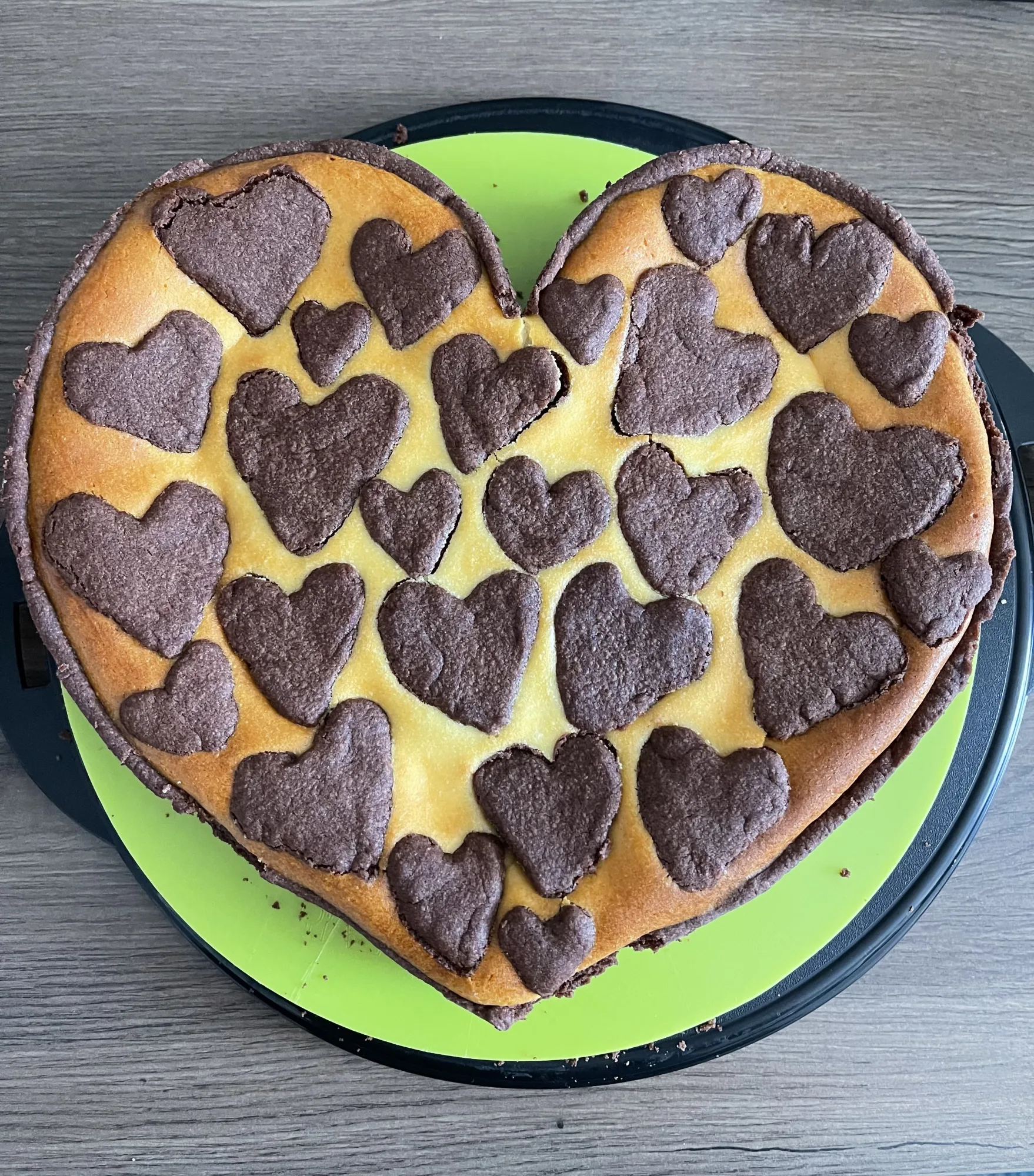 Herzförmiger Zupfkuchen mit goldgelber Quarkmasse, belegt mit vielen kleinen Schoko-Mürbeteigherzen, auf grüner Platte.