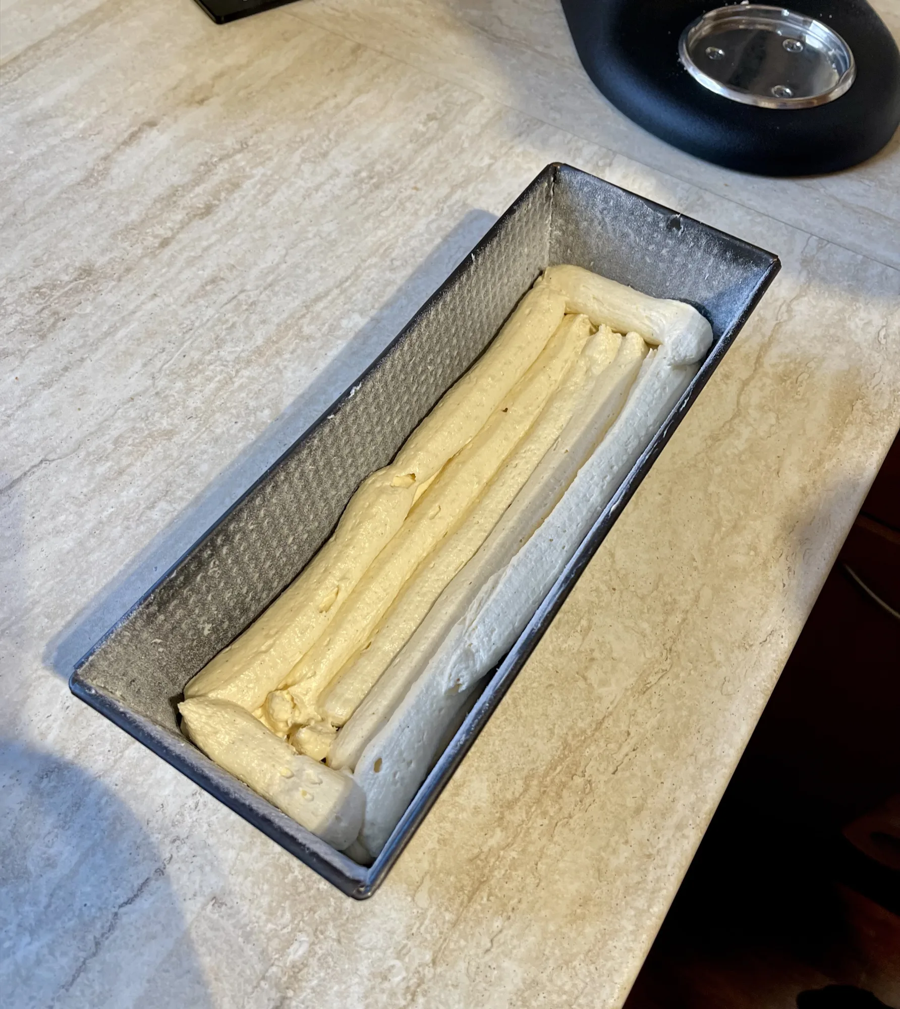 Kastenform mit ungebackenem Teig für den Kuchen mit verstecktem Herz: gelbe und weiße Teigstreifen liegen längs nebeneinander.