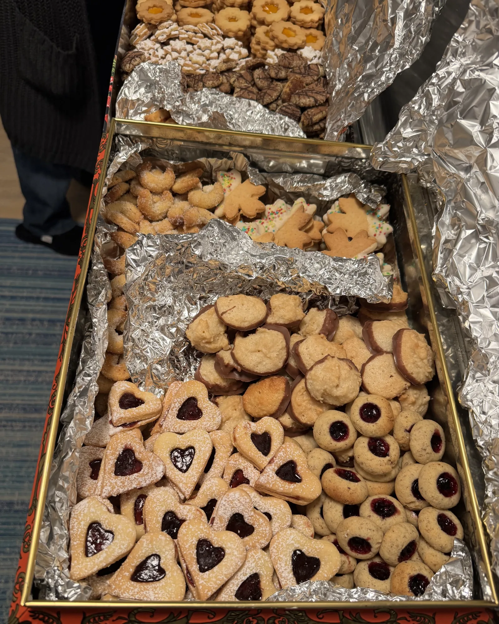 Zwei Blechdosen mit Alufolie voller Weihnachtsplätzchen: Linzer Herzen, Husarenkrapfen, Kokosmakronen mit Schokorand, Vanillekipferl.