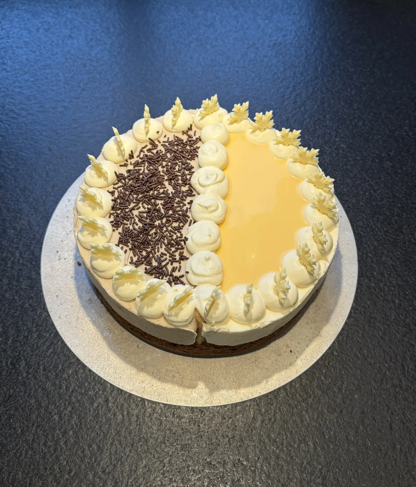 Sahnetorte halb/halb: eine Hälfte mit Schokostreuseln, die andere mit gelbem Guss, Sahnetupfen und weißen Schokoblättern am Rand.
