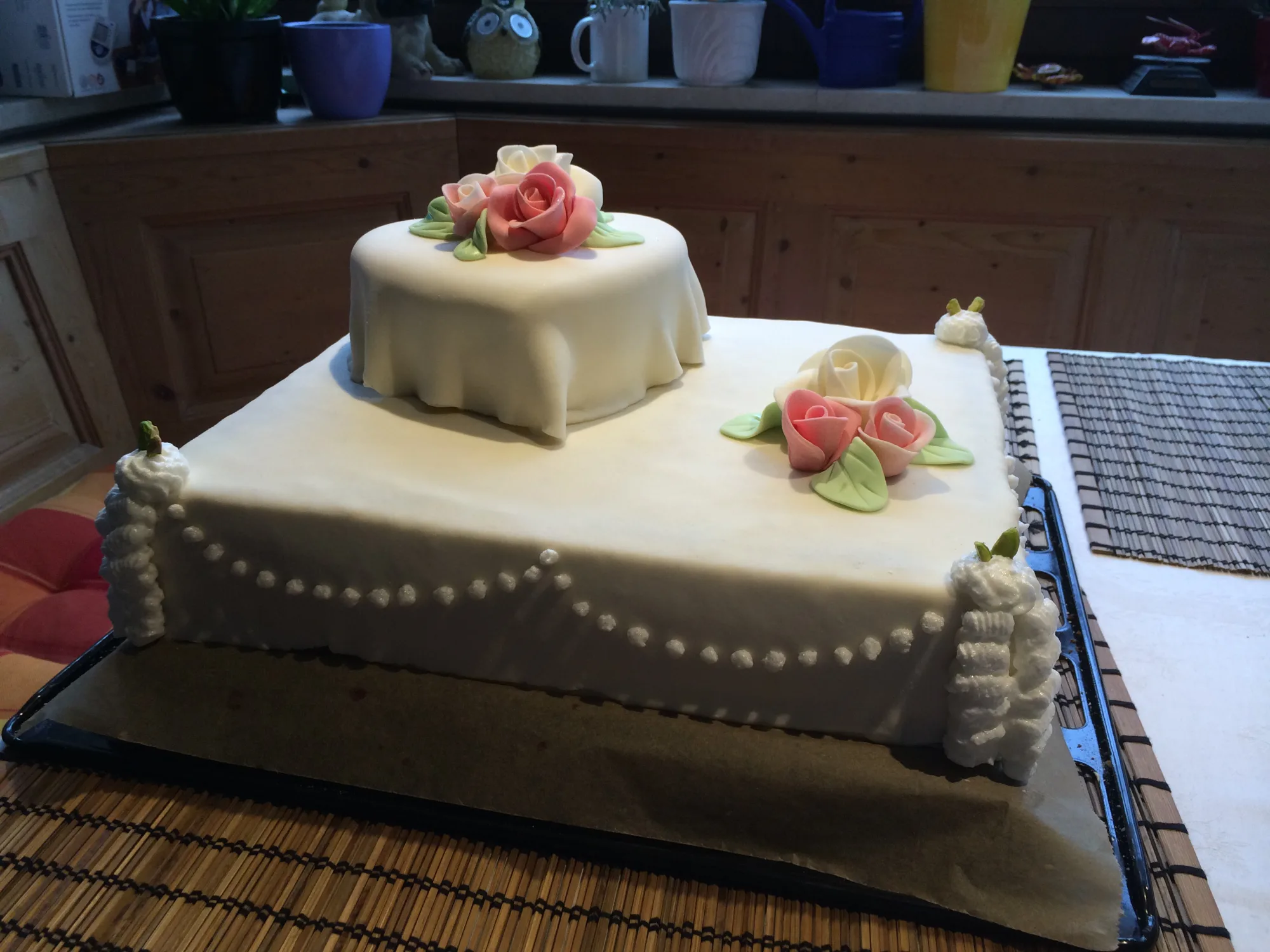 Hochzeitstorte mit weißem Fondant, herzförmigem Aufsatz, rosa und weißen Zuckerrosen, Perlenmuster und Cremetupfen an den Ecken