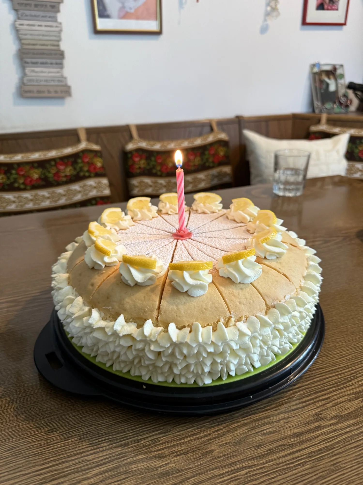 Torte mit Sahnetupfen, Zitronenscheiben und brennender rosa Kerze, vorgeschnitten, auf einem Holztisch in einer Stube