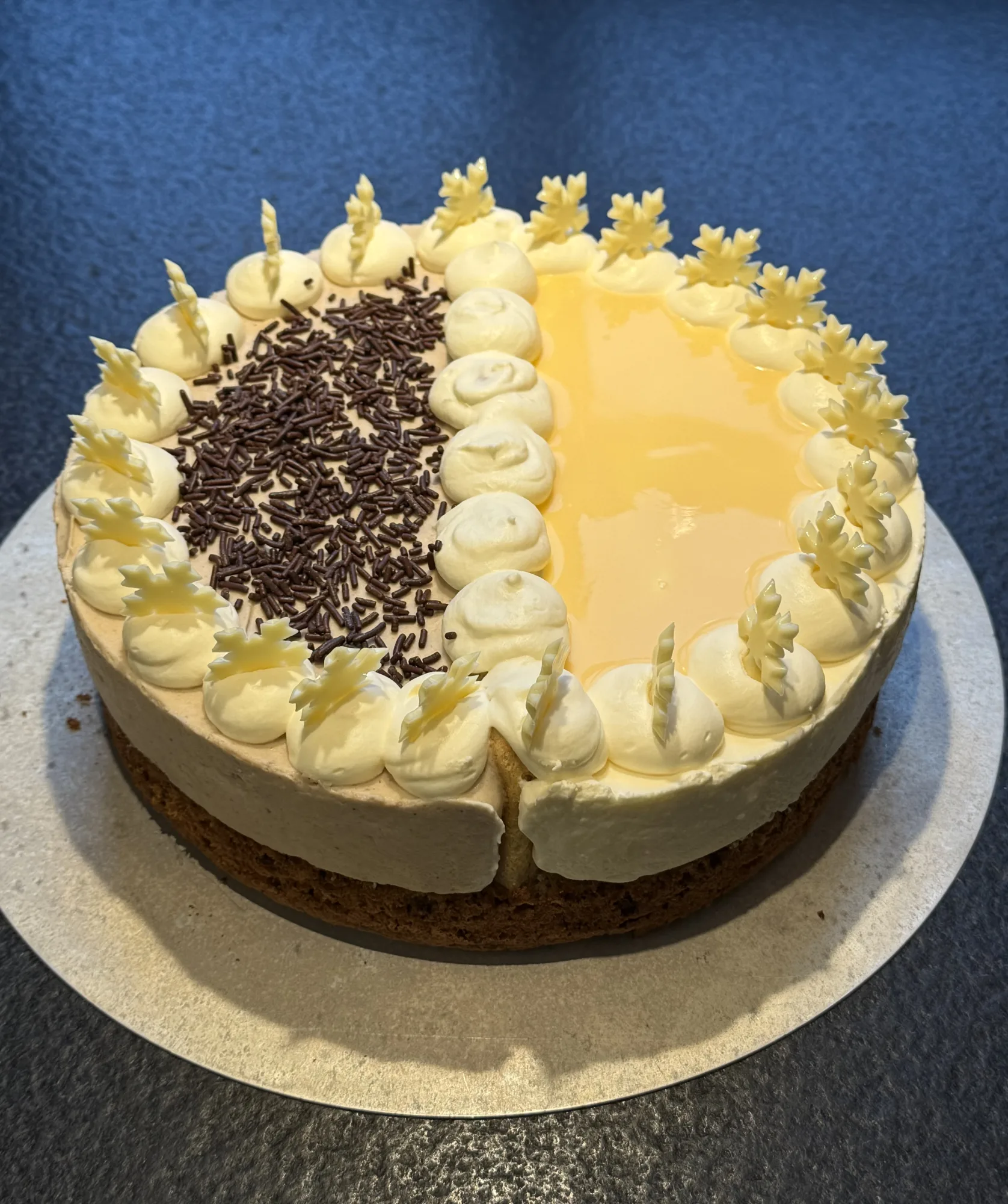 Sahnetorte halb/halb: eine Hälfte mit Schokostreuseln, die andere mit gelbem Guss, Sahnetupfen und weißen Schneeflocken aus Schokolade.