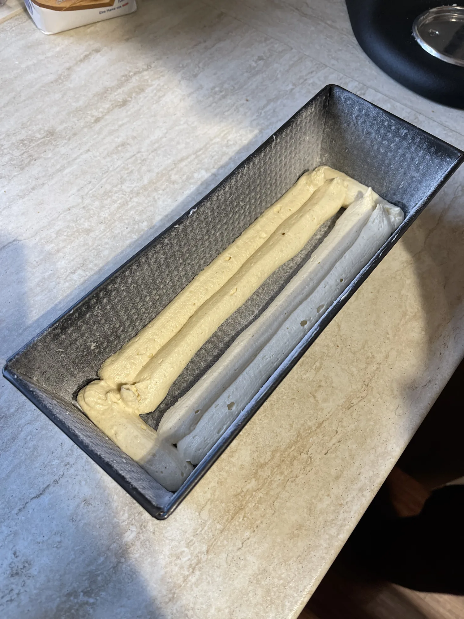 Kastenform mit zwei Teigsorten für den Kuchen mit verstecktem Herz: helle und gelbe Teigstränge liegen in einer V-Form auf dem Boden.
