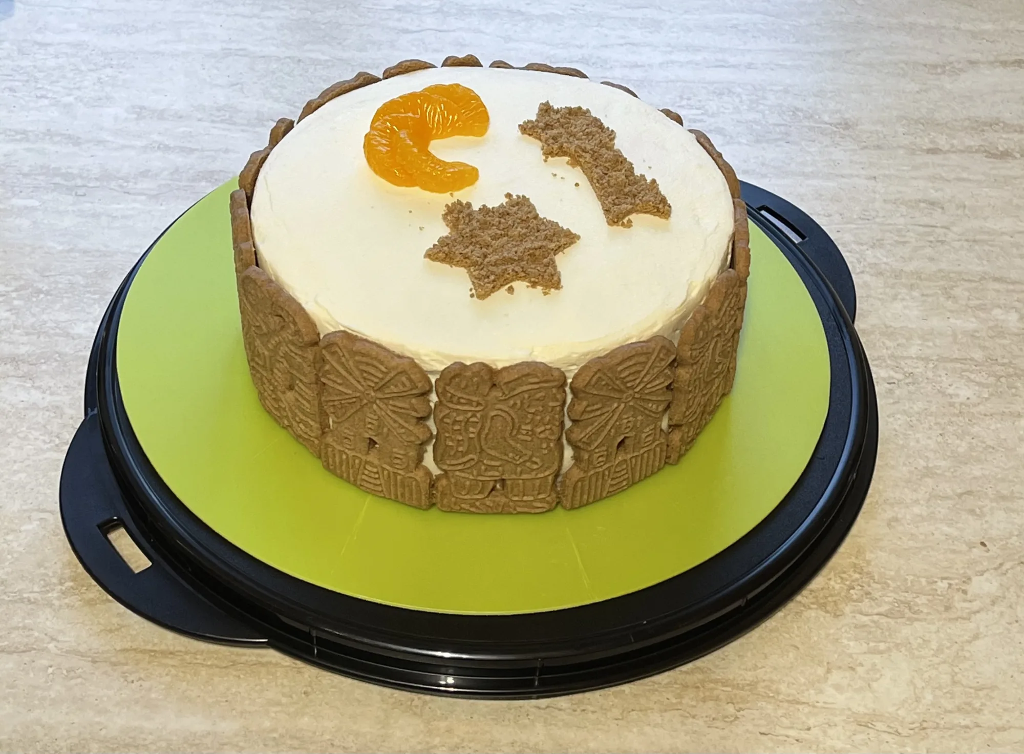 Kleine Torte mit heller Creme, Speculatiusrand, Mandarinenspalte und Gebäckstücken in Sternform auf grüner Platte