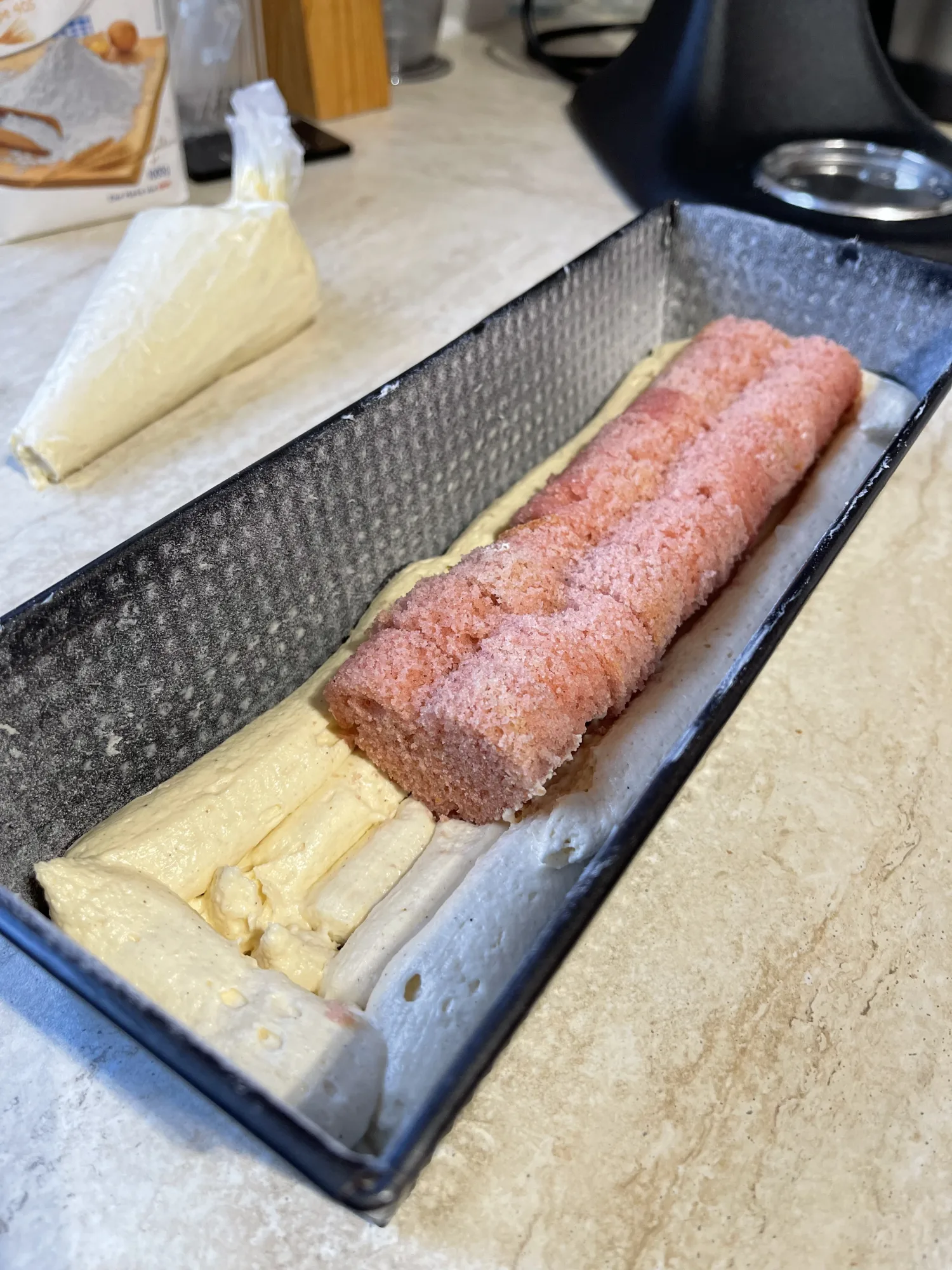 Kastenform mit hellem Rührteig, in dessen Mitte ein rosa Biskuitstreifen für den Kuchen mit verstecktem Herz liegt