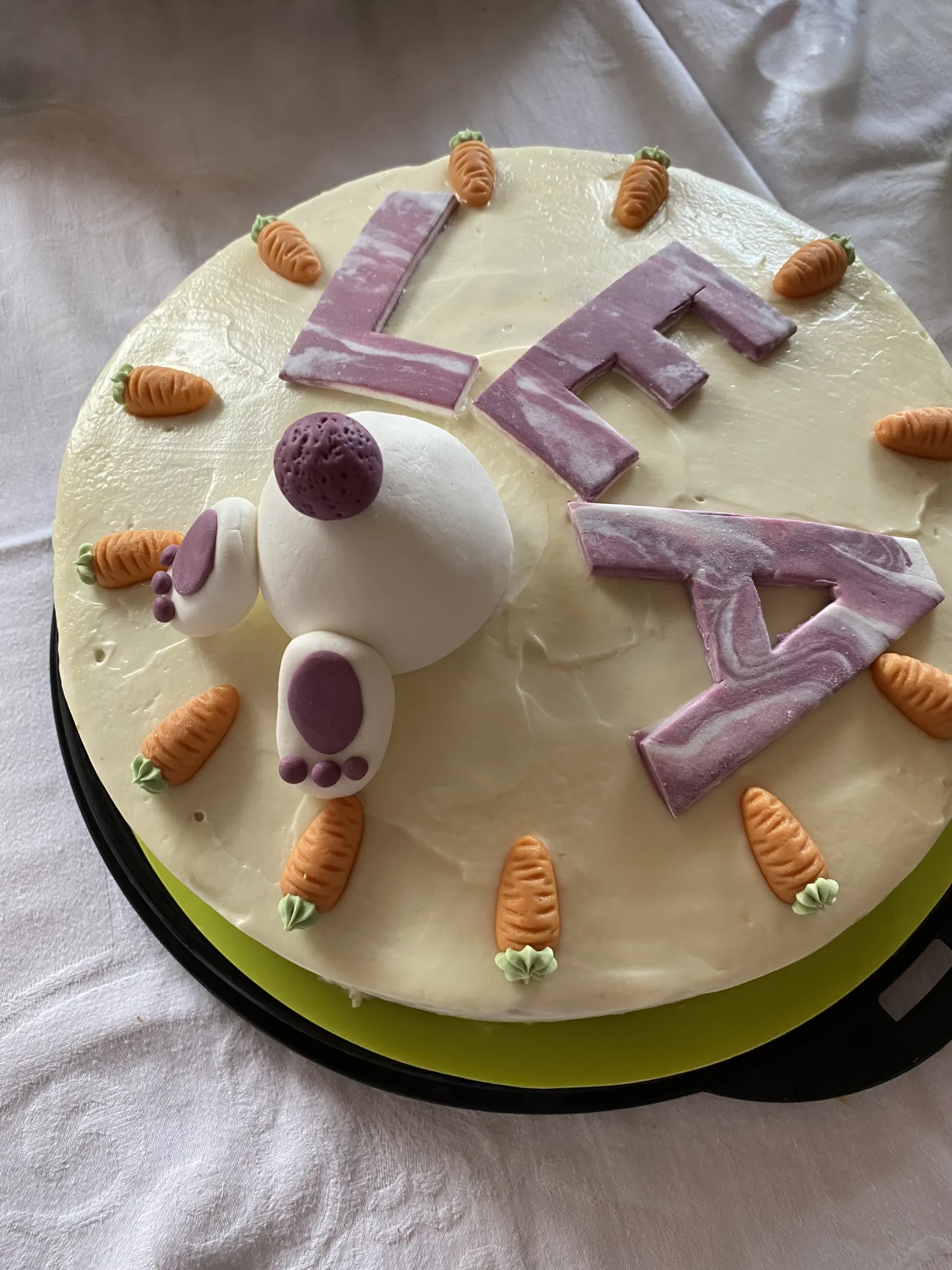 Namenstorte mit heller Creme, lila marmorierten Fondantbuchstaben „LEA“, Fondant-Hasenpo mit Pfoten und Marzipanmöhrchen am Rand