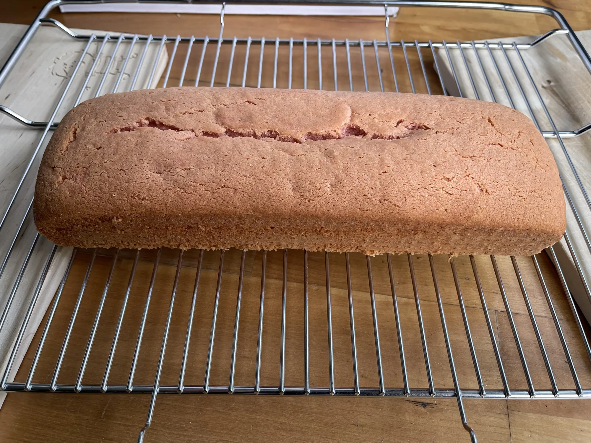 Rosafarbener Kastenkuchen mit eingerissener Oberseite kühlt auf einem Abkühlgitter über einem Holztisch, Kuchen mit verstecktem Herz.