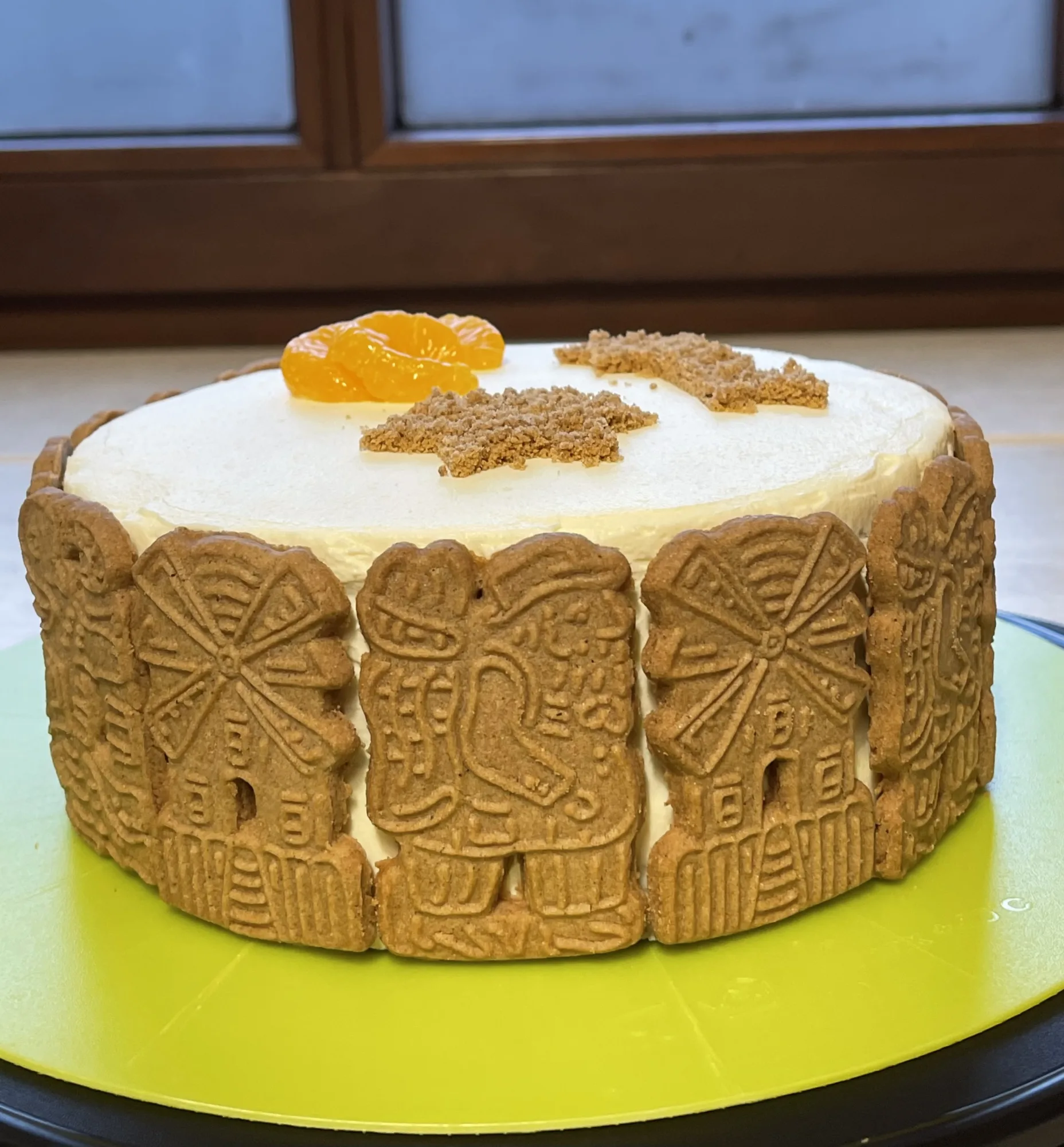 Kleine Torte mit heller Creme, Spekulatius-Rand, Mandarinenspalten und Keksbröseln auf einer grünen Drehplatte