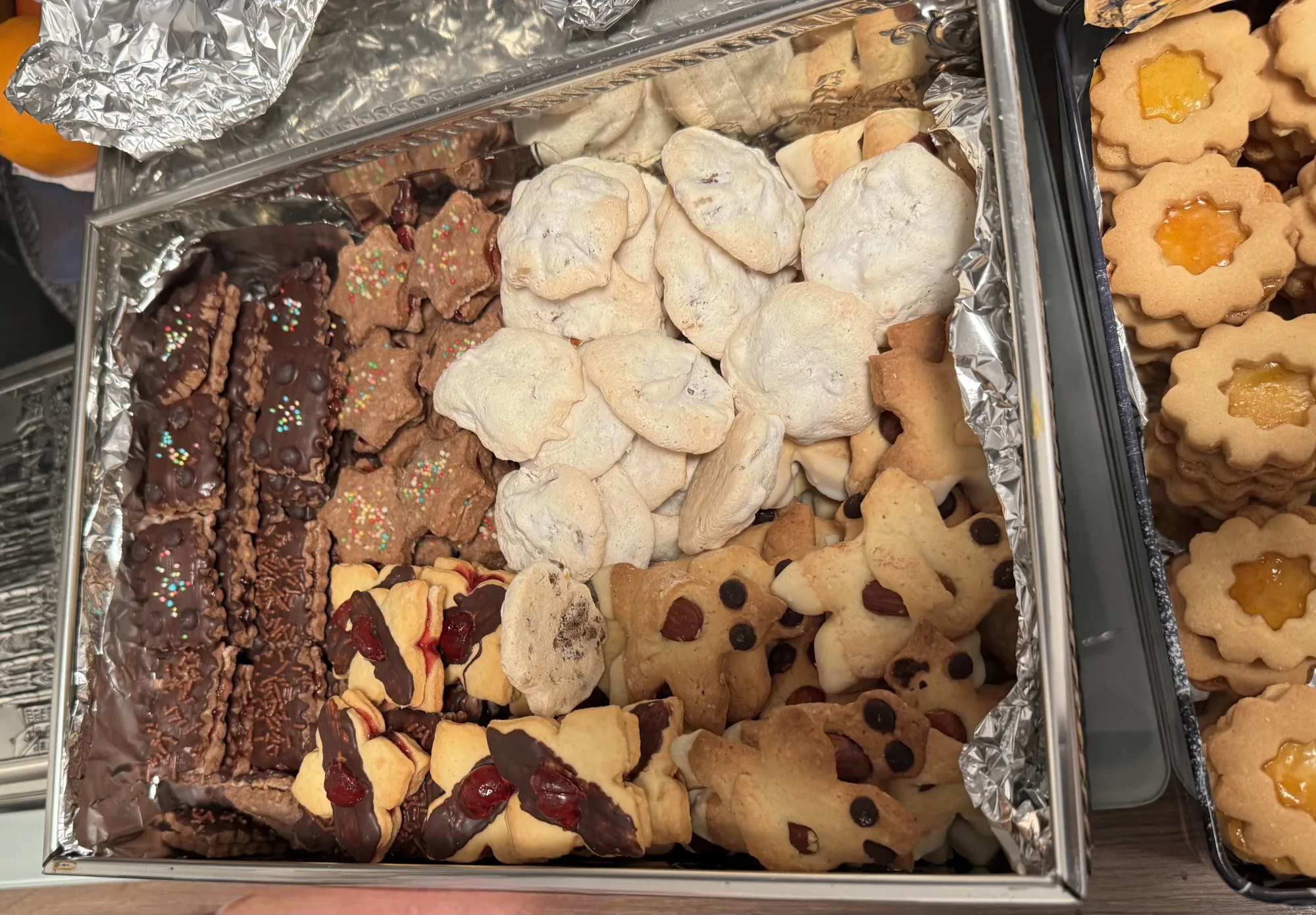 Weihnachtsplätzchen in einer mit Alufolie ausgelegten Blechdose: Baisers, Schoko-Schnitten, Sterne, Männchen, daneben Linzer Augen