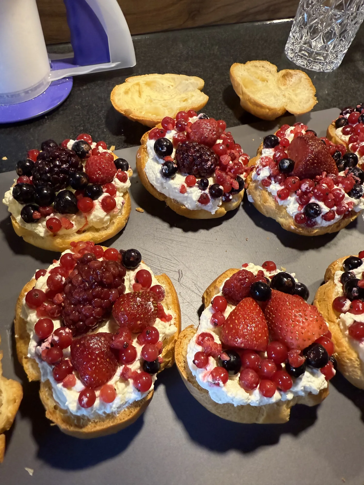 Aufgeschnittene Windbeutel-Böden mit Sahnecreme, Erdbeeren, Brombeeren, Johannisbeeren und Heidelbeeren auf einem Blech