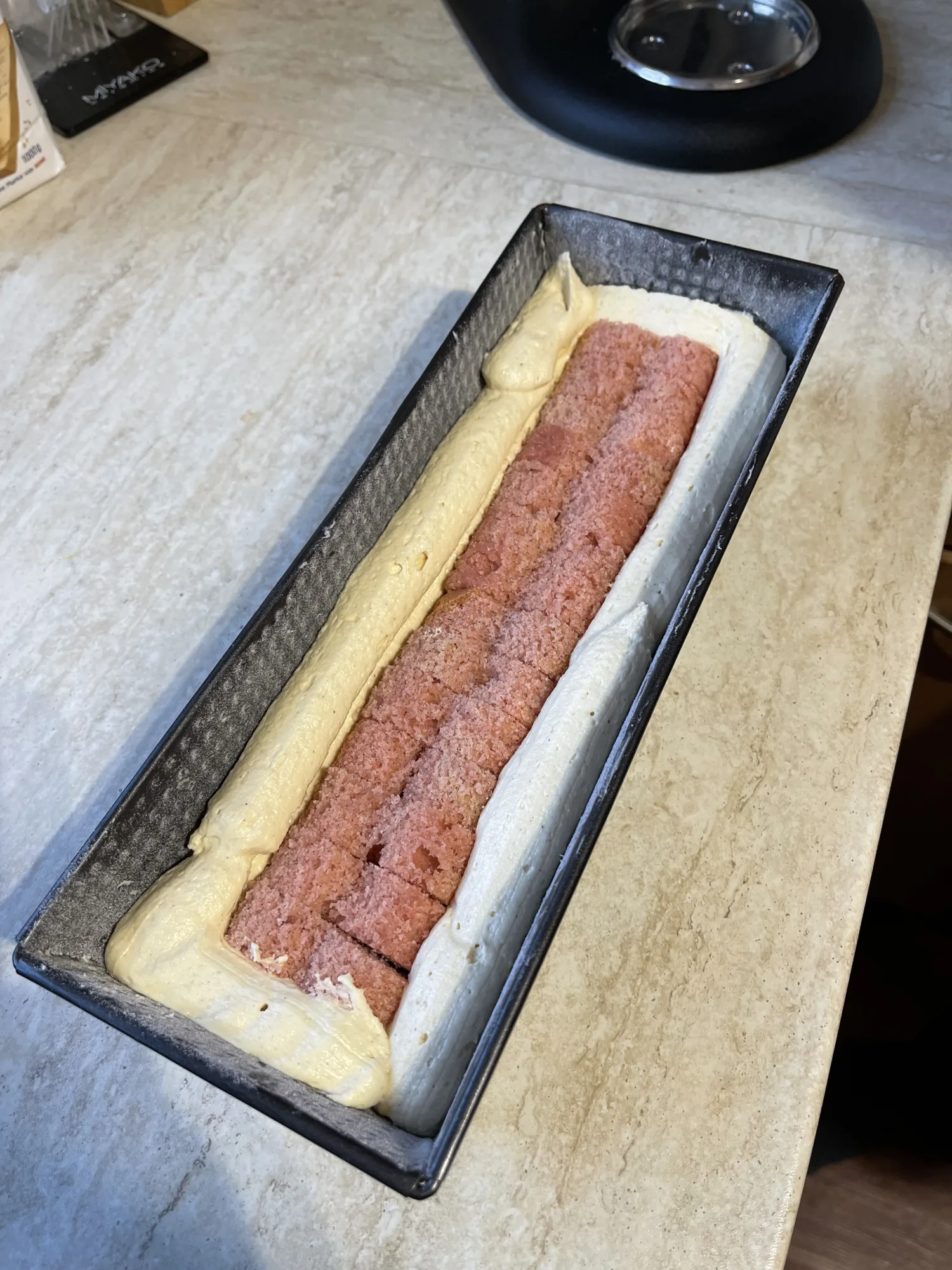 Kastenform mit hellem Rührteig, in dessen Mitte rosa gefärbte Kuchenstücke für den Kuchen mit verstecktem Herz gereiht sind