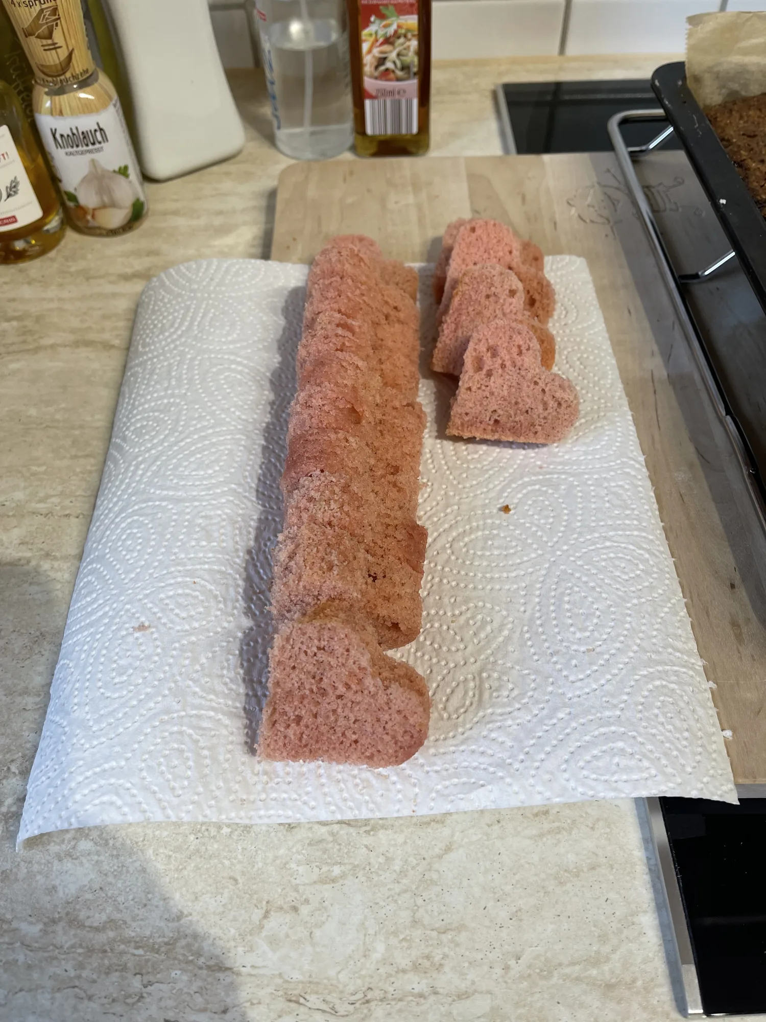 Rosa Rührkuchen, in Herzen ausgestochen und hochkant in zwei Reihen auf Küchenpapier für den Kuchen mit verstecktem Herz aufgereiht