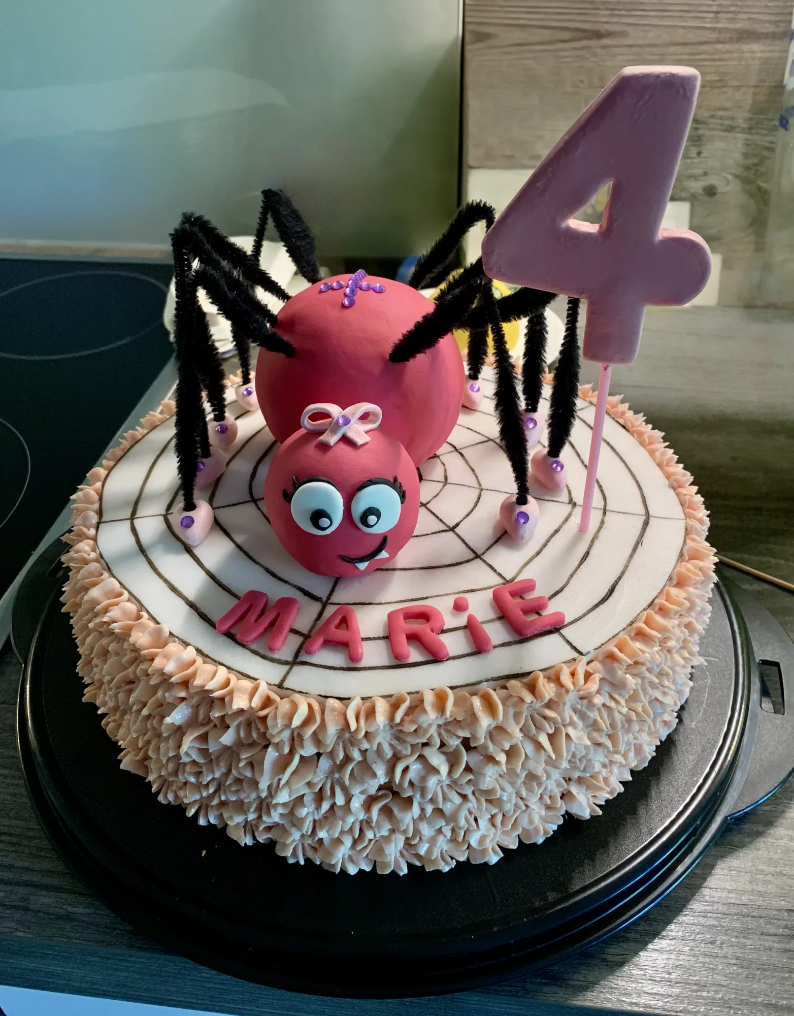 Namenstorte mit rosa Fondant-Spinne auf aufgemaltem Spinnennetz, Schriftzug „Marie“, rosa Zahl 4 und Rand aus Cremetupfen