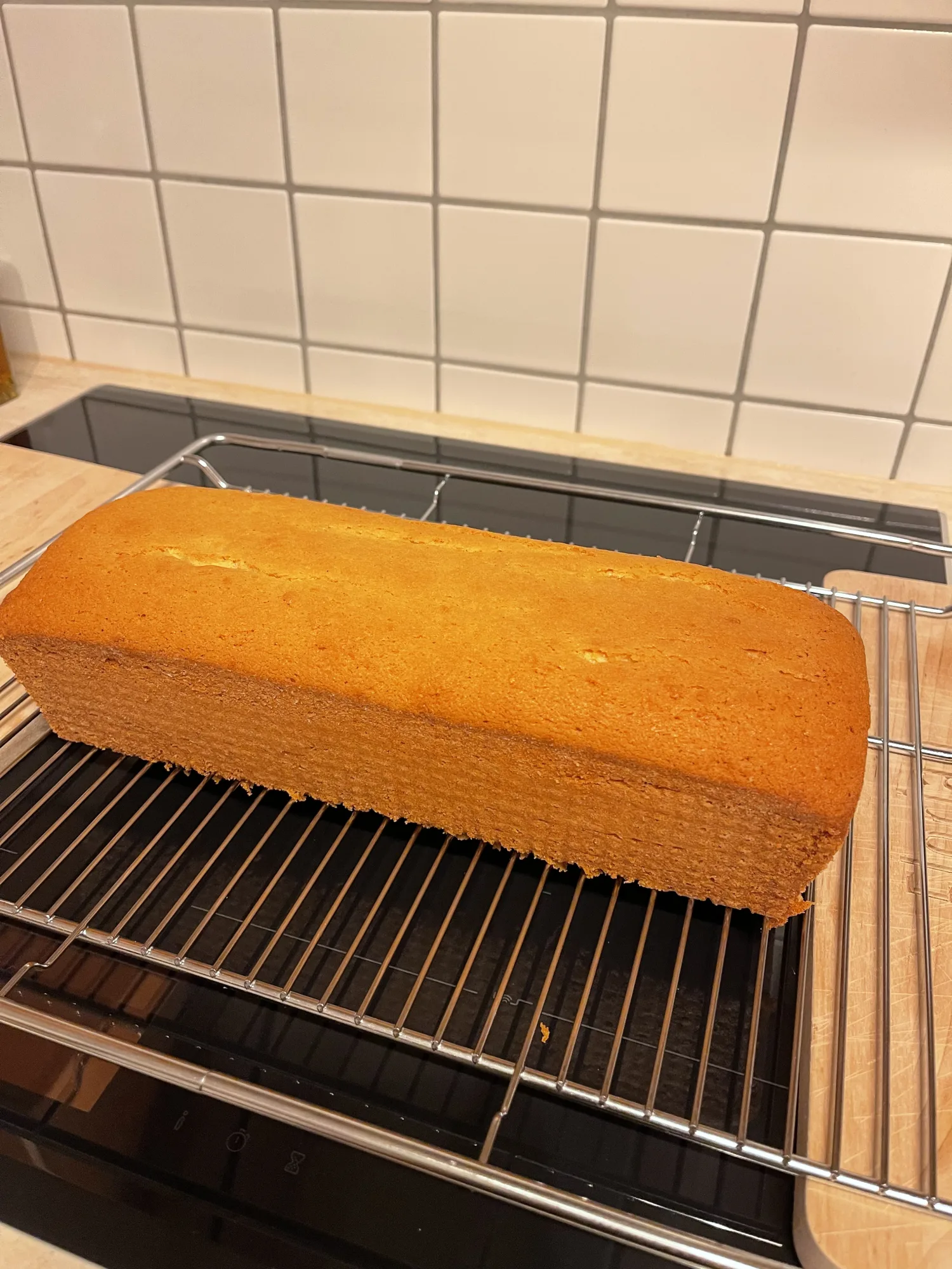 Goldbrauner Rührkuchen aus der Kastenform liegt zum Auskühlen auf einem Gitterrost auf dem Herd, dahinter weiße Fliesen.