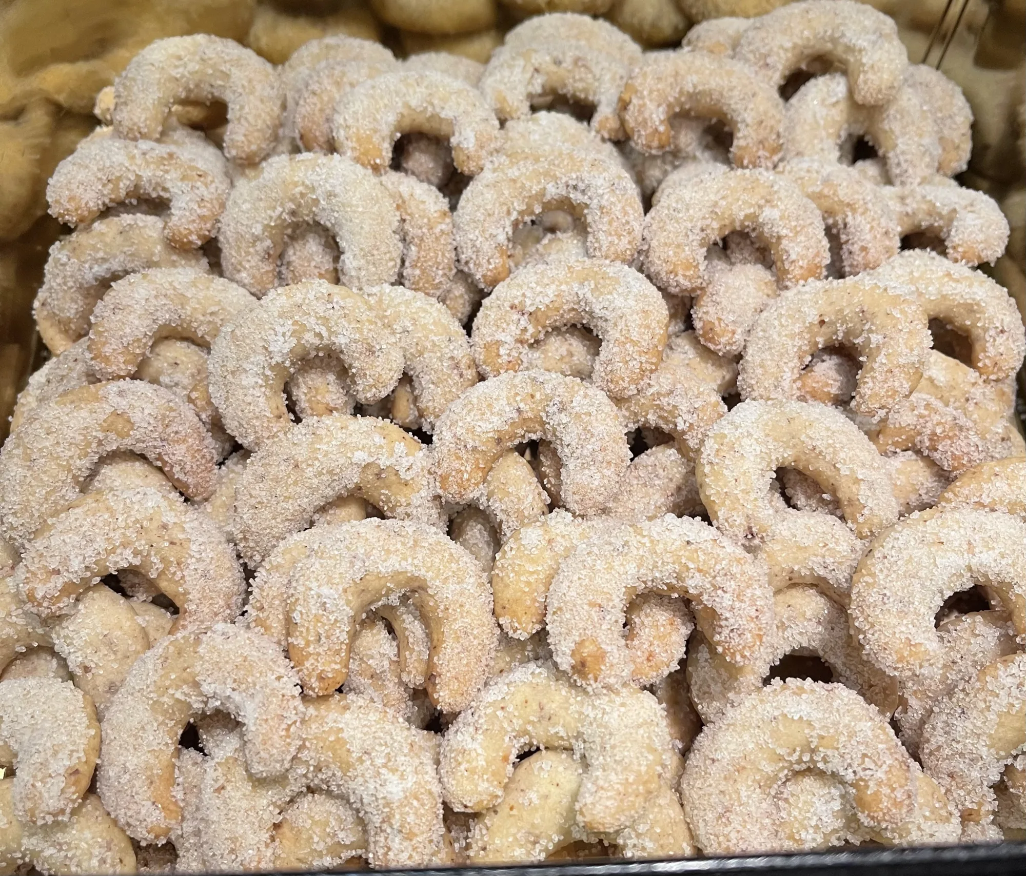 Vanillekipferl, dicht gestapelt in einer Dose, mit grobkörnigem Zucker bestreut und leicht goldbraun gebacken.