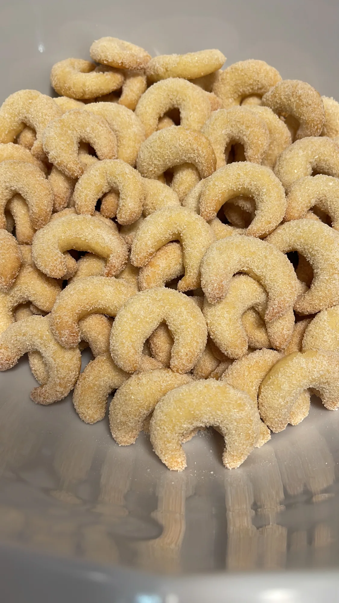 Vanillekipferl, dick mit Zucker bestreut, liegen aufgehäuft in einer grauen Schüssel, in der sich das Gebäck spiegelt.