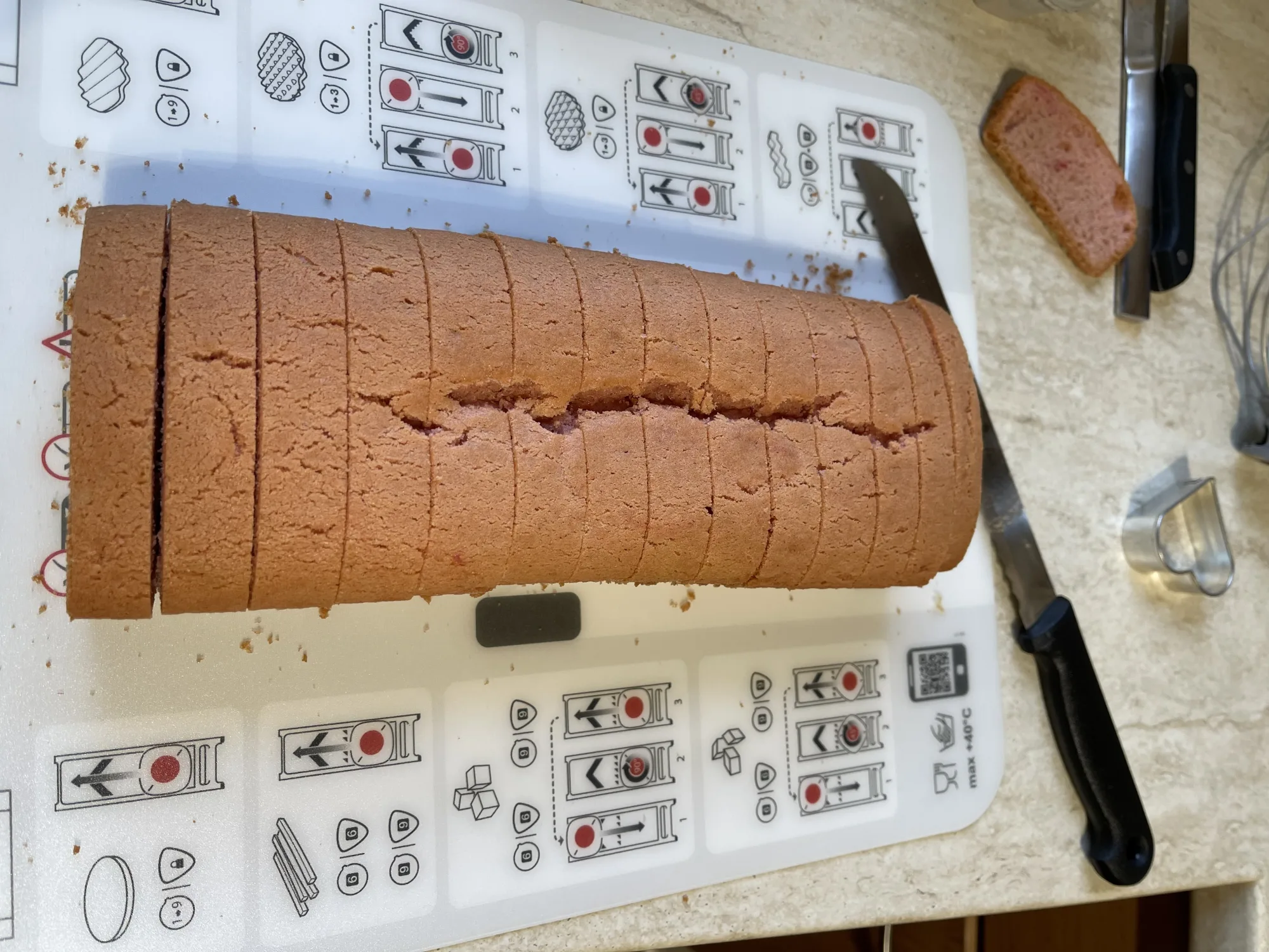 Rosa Kastenkuchen mit Längsriss, in Scheiben geschnitten, auf weißer Schneidunterlage; daneben Brotmesser und eine einzelne Scheibe.