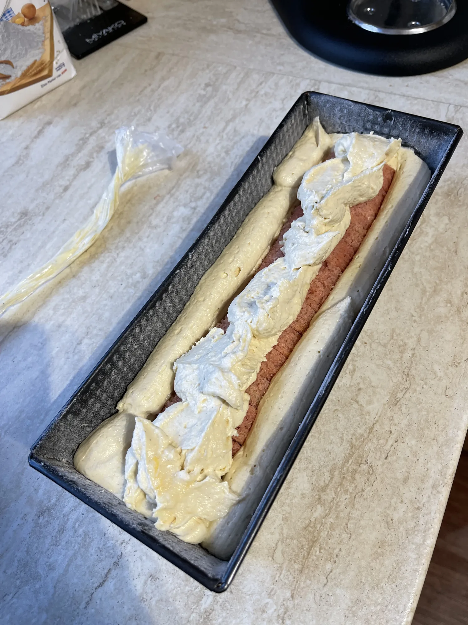 Kastenform mit hellem Rührteig, in der Mitte ein rosa Kuchenstrang, darauf Teig gestrichen – Kuchen mit verstecktem Herz.