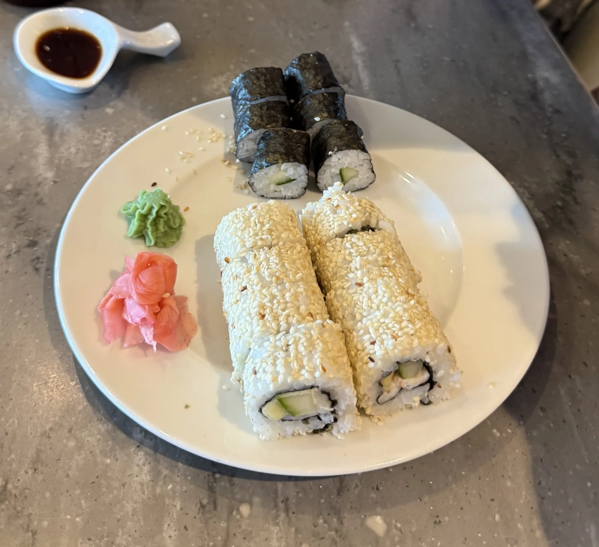 Sushi rice as cucumber maki and sesame-coated uramaki on a white plate with wasabi, pickled ginger and soy sauce