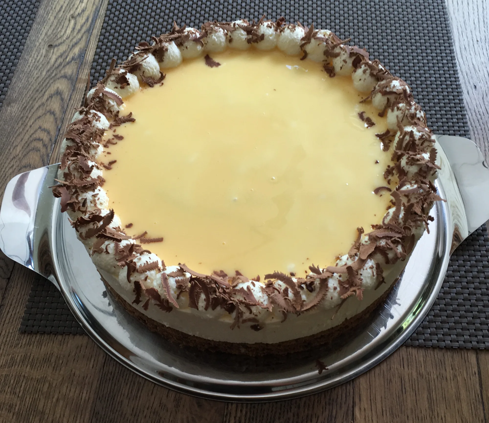Eggnog liqueur cream cake with a smooth yellow top, piped cream dots and chocolate shavings on the rim, on a metal platter